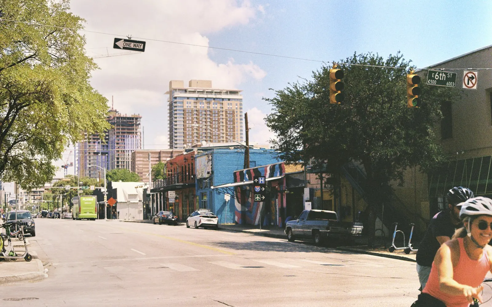 A cyclist waits at traffic lights on a sunny Austin street lined with low-rise buildings
