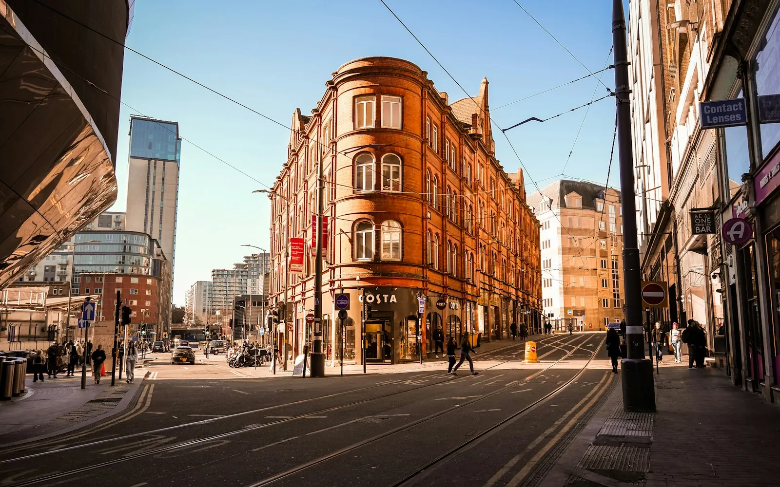 A sunny Birmingham city centre street with a red-brick Victorian corner building