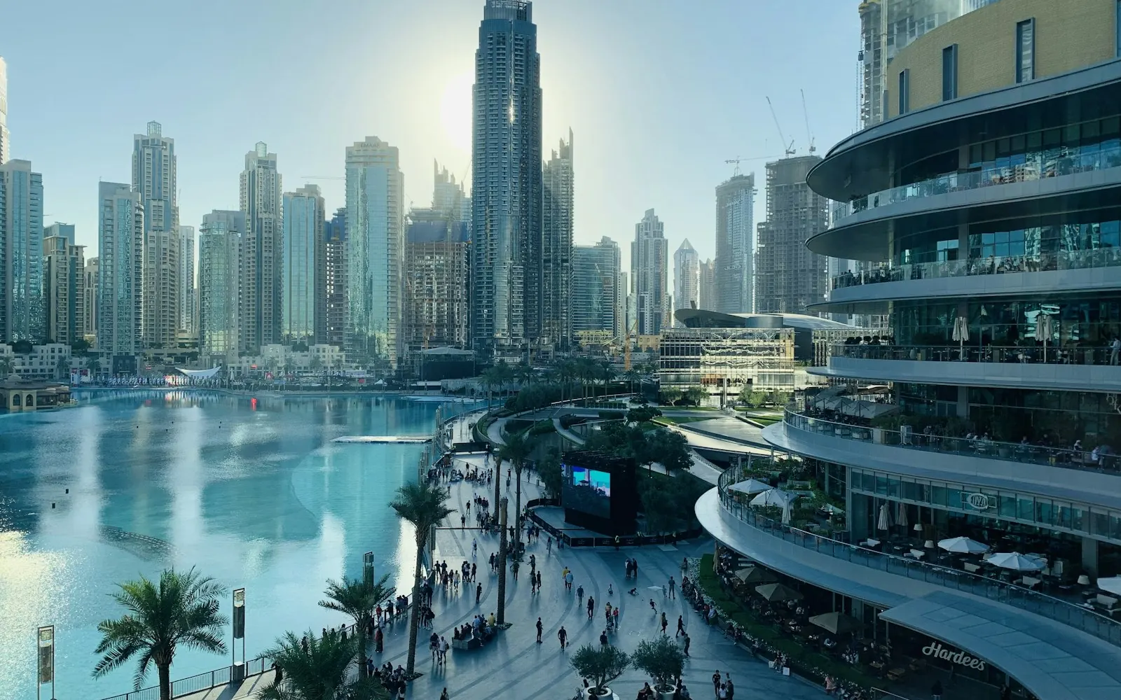 People walking along the palm-lined Dubai Marina promenade beneath tall residential towers