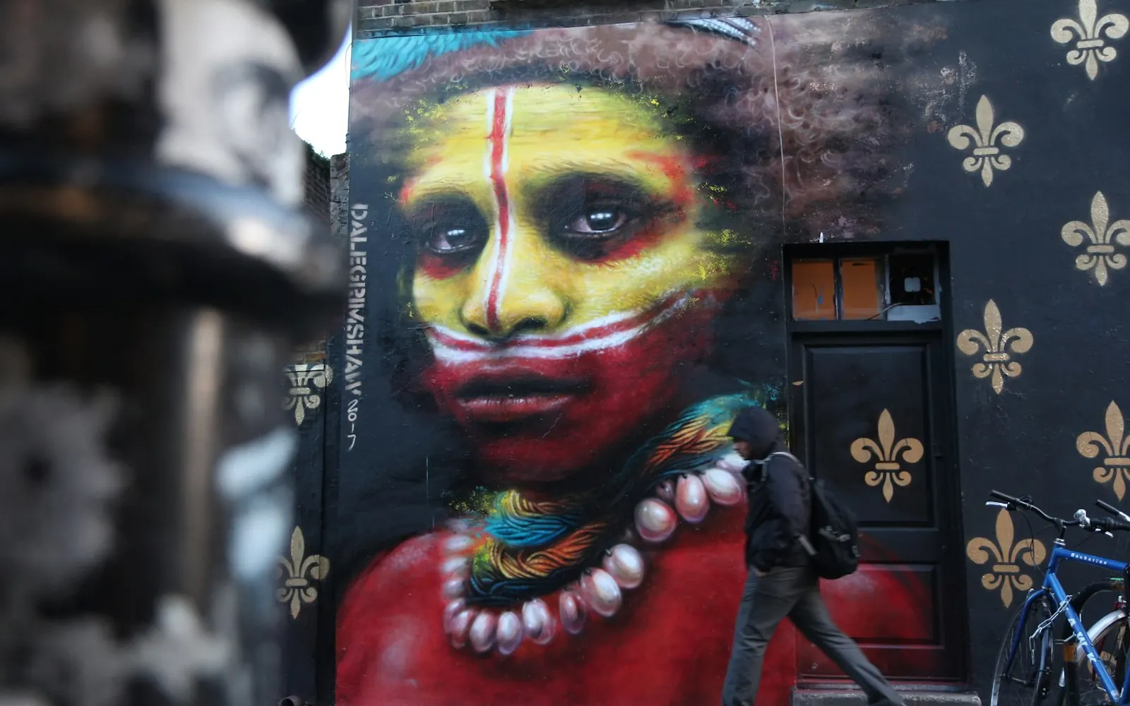 A person walking past a large, colourful street-art mural on an East London street in Shoreditch