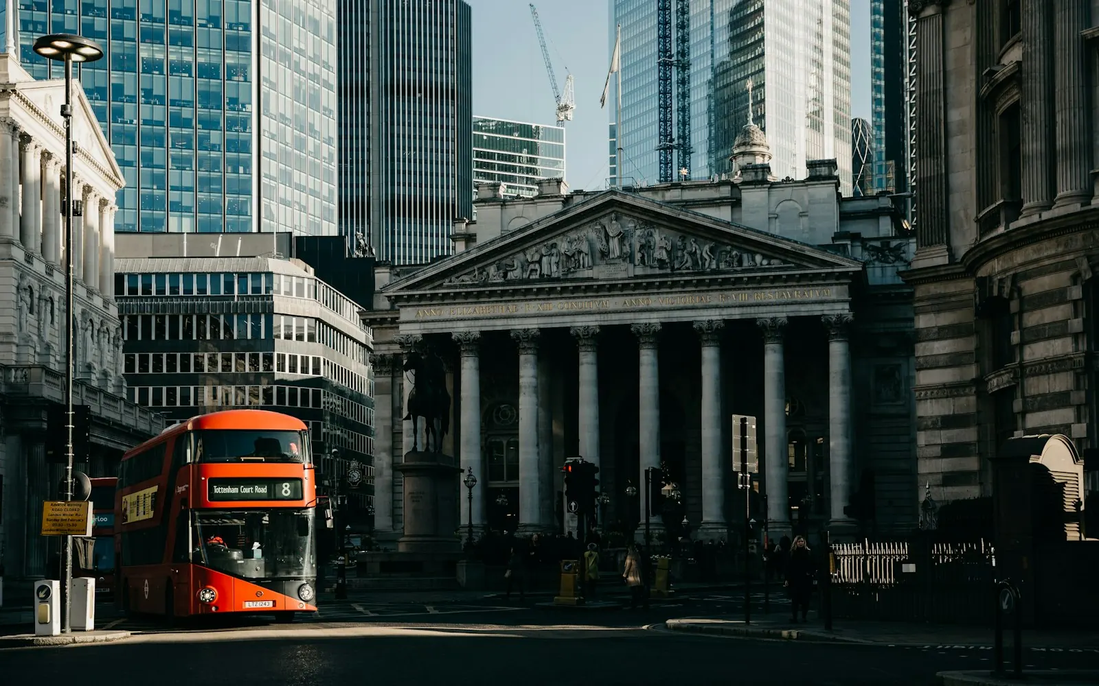 A red double-decker bus passing the Royal Exchange at Bank junction with City of London towers behind
