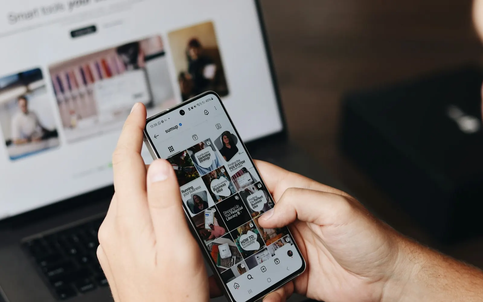 A hand scrolling a photo grid on a phone in front of a laptop during Sydney social planning