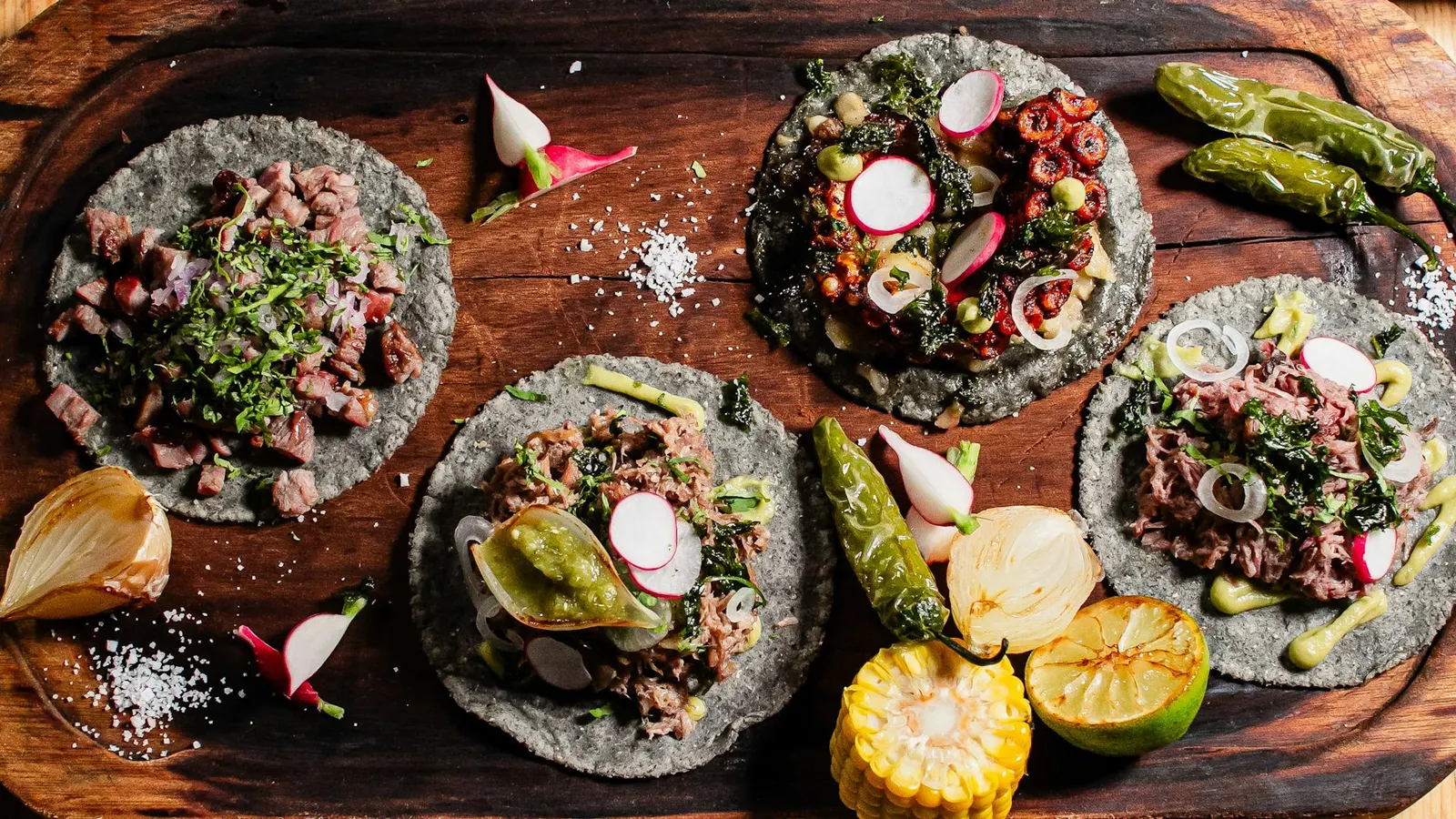 Four tacos with assorted toppings on a wooden board