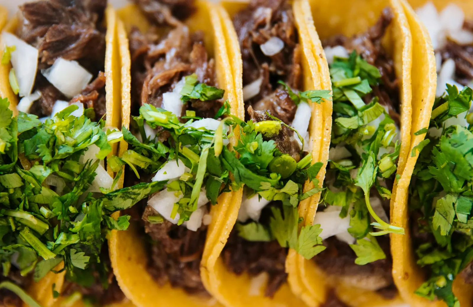 Three beef street tacos topped with onion and fresh coriander