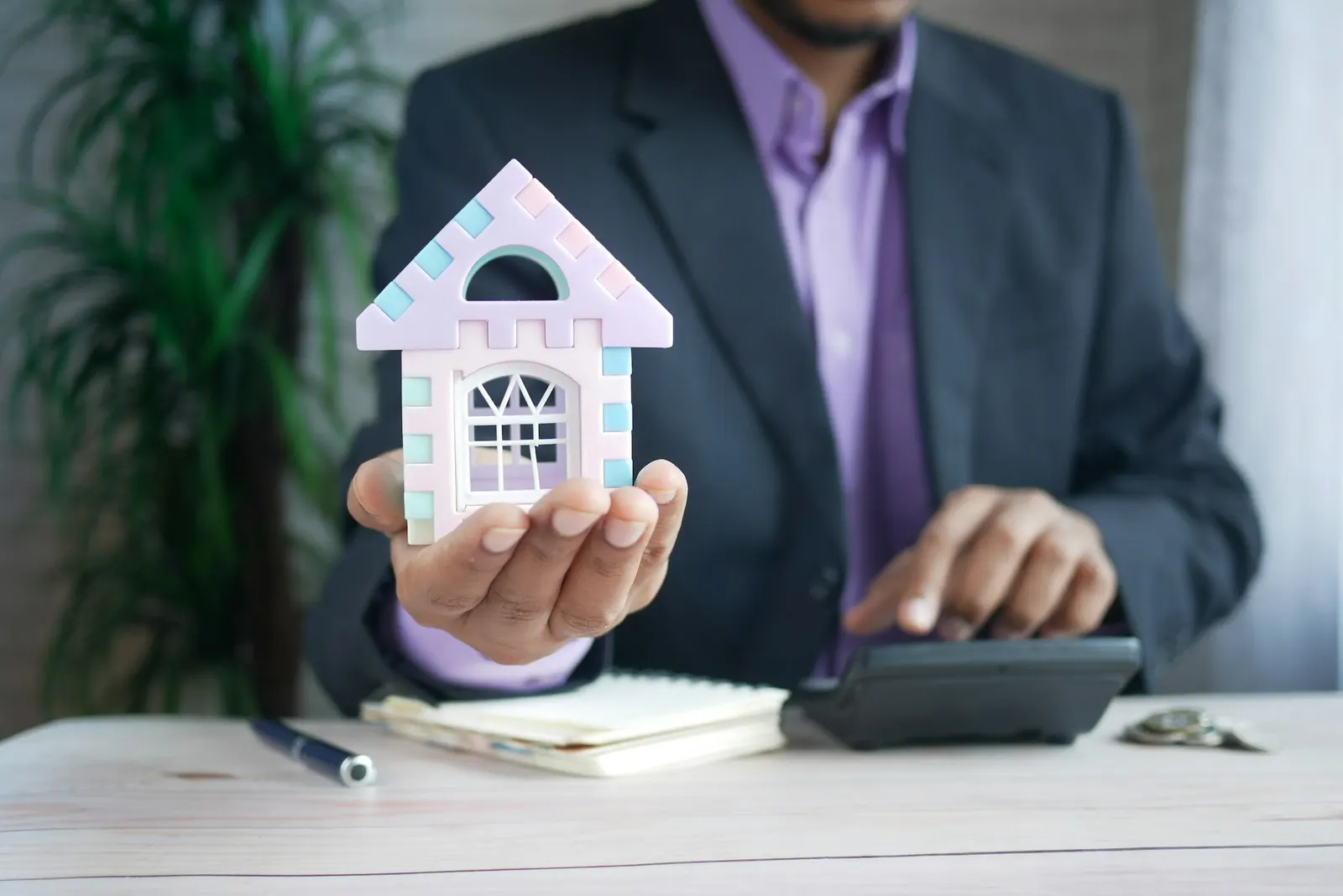 An adviser holding a small model house over a desk with a calculator