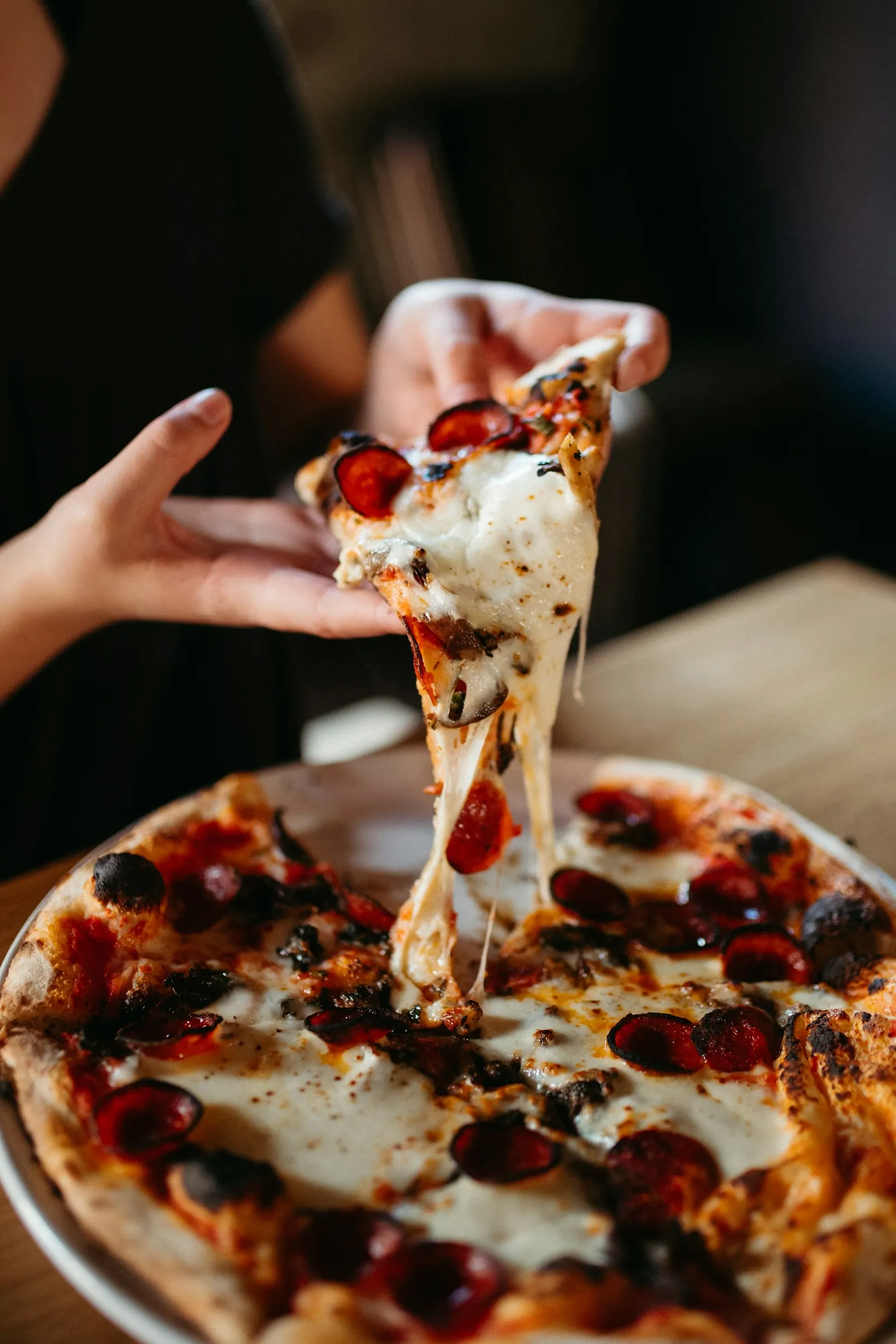 A hand lifting a cheesy slice from a fresh pizza