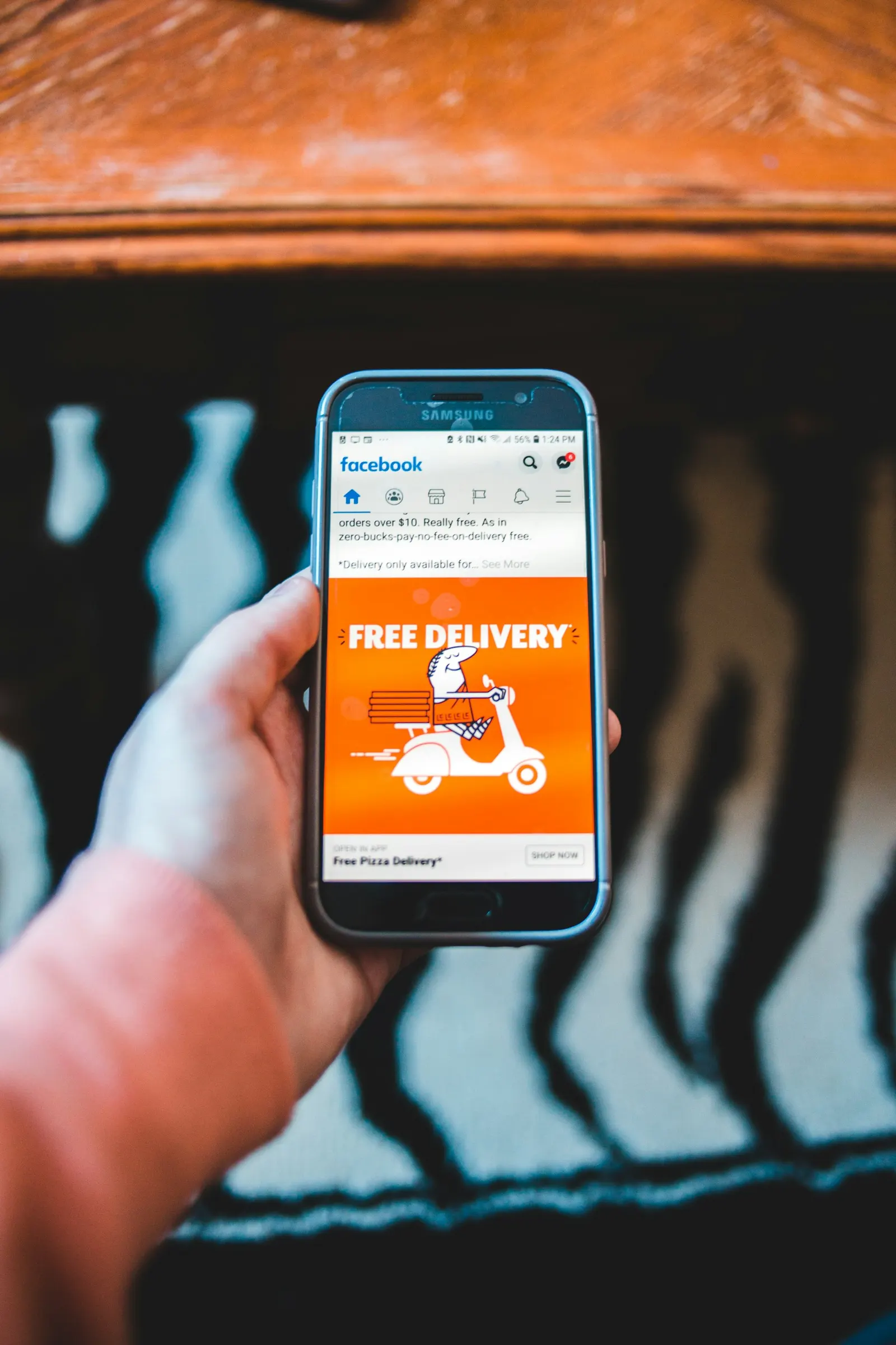 Hand holding a phone showing a sponsored post with a free delivery offer